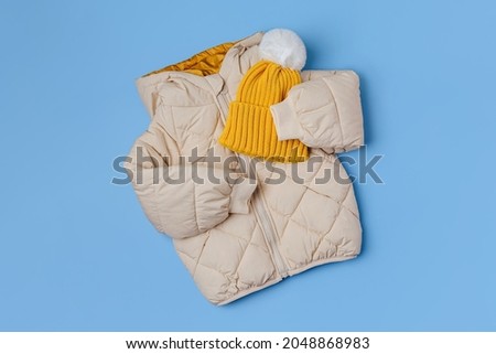 Kids warm puffer jacket with yellow  hat on blue background. Stylish childrens outerwear. Winter fashion outfit  Royalty-Free Stock Photo #2048868983