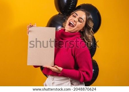 Charming smiling young woman with banner with free space for text and balloons on black background. Black friday promotion concept