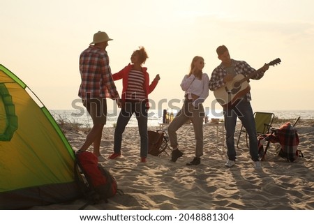 Friends having party near camping tent on sandy beach