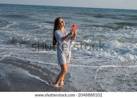 Young woman taking pictures of herself against the background of the sea.