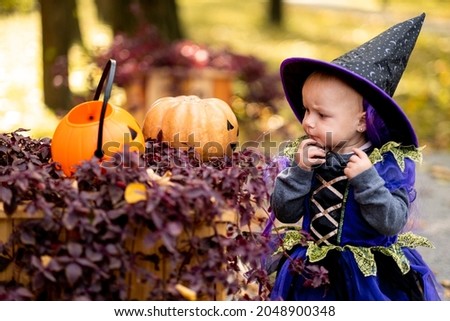 Happy Halloween Cute little witch with pumpkins. Beautiful young child girl in suit outdoors.