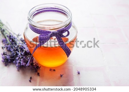 Jar with honey and fresh lavender flowers on a tile background
