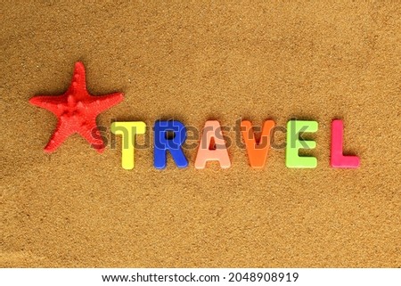 On the beach sand is written a word of bright letters the word travel.