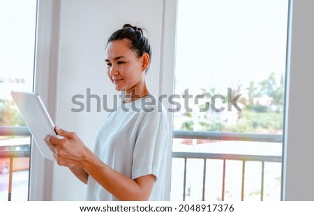 Pretty Asian Woman using tablet computer, standing by the bright window. Copy space