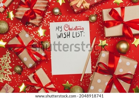 Festive layout of holiday decorations, confetti, toys and gift boxes with christmas wish list on red paper background. Above view, flat lay.