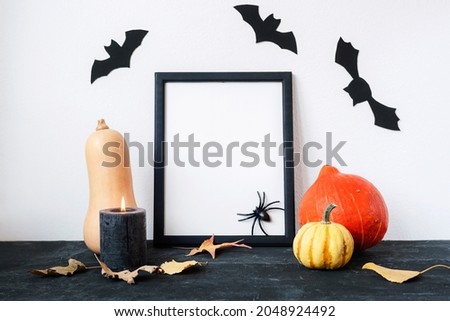 Halloween holiday concept with blank picture frame, pumpkins, candle, bats and spider on black and white background. Mock up.