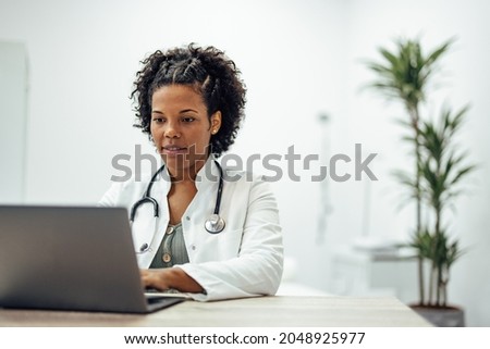 Smiling doctor using laptop while working in private practice. Royalty-Free Stock Photo #2048925977