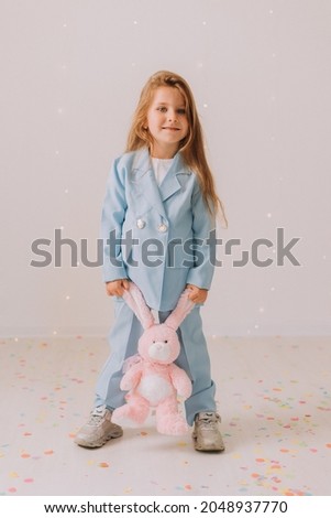 little girl in a business blue pantsuit with a toy rabbit in her hands stands on a gray background. educational concept. poster, banner. Space for text. High quality photo