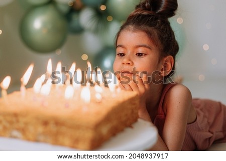 Little dark-skinned girl makes a wish and blows out the candles on the birthday cake. Cute girl celebrating her birthday