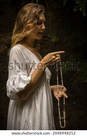 Caucasian woman keeping count during pray and meditation. Buddhist japa mala. Strands of gemstones beads. Religion concept. Buddhist jewelry. Woman wearing white dress. Bali, Indonesia
