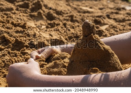 the child's hands are raking sand to build a sand castle