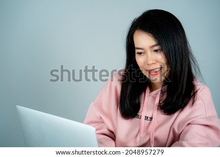 Portrait of an Asian girl wearing a pink shirt. sitting on a laptop computer online shopping with a happy face behind a gray studio background