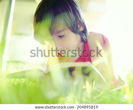Kid reading book on summer grass meadow