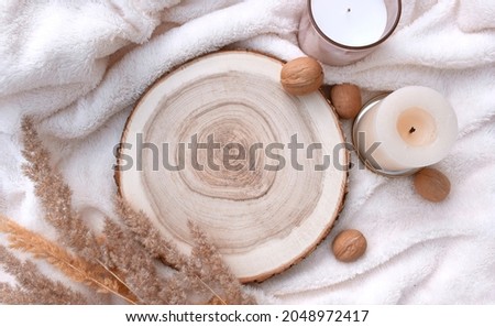 Cozy winter mockup still life scene with wooden round tray, candles and walnuts on white plaid. Nordic home decor flat lay for Christmas holidays or Thanksgiving. Trendy eco layout concept. Royalty-Free Stock Photo #2048972417