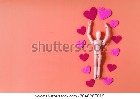 A mannequin of a wooden man with his hands raised above his head, surrounded by red and pink hearts. Valentine's Day greeting card man and hearts on a red background.