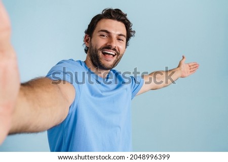 Young brunette man showing copyspace while taking selfie photo isolated over blue background
