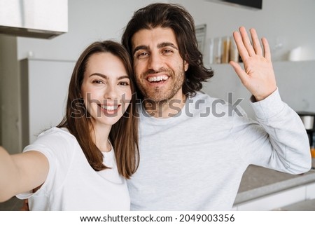 Young multiracial couple gesturing and hugging while taking selfie photo at home