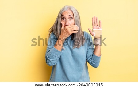 middle age pretty woman covering mouth with hands with a shocked. hand bandage concept
