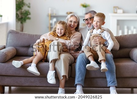 Happy family joyful little children hugging embracing with positive senior grandparents while sitting together on sofa in living room at home, cheerful grandma and grandpa with kids smiling at camera Royalty-Free Stock Photo #2049026825