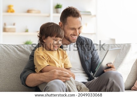 Modern technologies and kids development. Happy young father watching cartoons on digital tablet, sitting together at home, free space