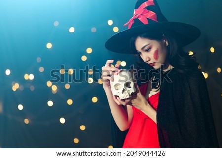 Portrait of beautiful young woman in witch halloween costume wear witches hat hold human skull over spooky dark magic background - Halloween party concept