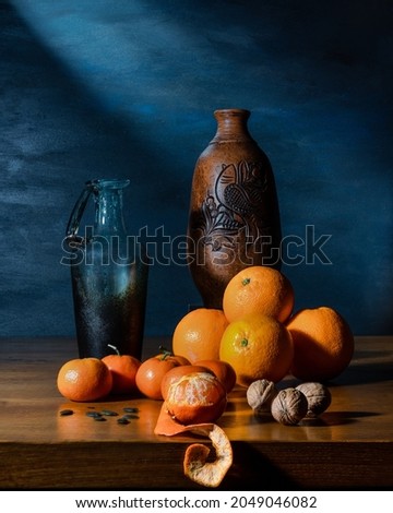 Still life with rustic vases, oranges, tangerines, nuts on a wooden table and blue background. Art photography. Front view, copy space