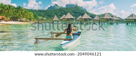 Bora Bora travel vacation iconic photo. Outrigger Canoe - woman paddling in traditional French Polynesian Outrigger Canoe. Mount Otemanu and overwater bungalow resort hotel sport lifestyle Royalty-Free Stock Photo #2049046121