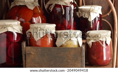 Assortment of canned preserves: fruit jam, compote, tomato paste and vegetable cans in the pantry on rustic wooden shelves, closeup, home storage organization concept