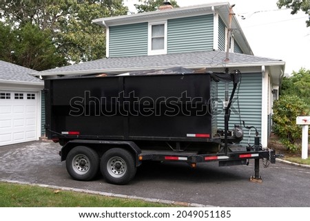 A contractors dumpster is on a trailer for easy hauling in their customers driveway. Royalty-Free Stock Photo #2049051185