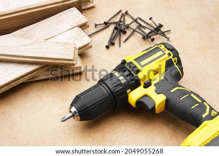Yellow-black screwdriver on wood background, screws. Parquet boards.