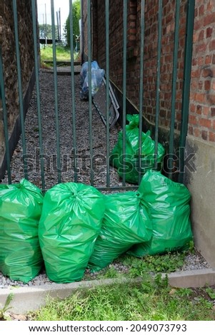 green bags stand in front of a metal gate