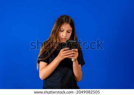 Wondering little cute girl surprised with an interesting information on mobile smartphone. Isolated on blue background.