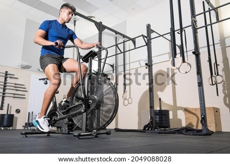 Fit man doing cardio training on stationary air bike machine with fan at the gym. High quality photo Royalty-Free Stock Photo #2049088028
