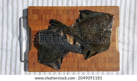 Two black flounders without a head on a wooden board. Recipes, cuisine, fishing.