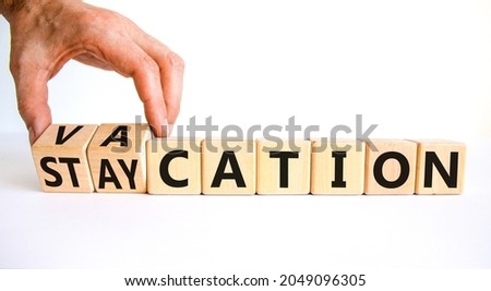 Vacation or staycation symbol. Businessman turns wooden cubes and changes the word vacation to staycation. Business and vacation or staycation concept. Beautiful white background, copy space.