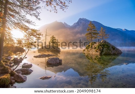 Majestic sunrise on Hintersee lake at autumn morning. Pine trees on stones reflected in the water. The fog spreads over the water. Magic painterly scene in Berchtesgaden Alps, Germany