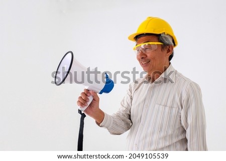A smiling senior wearing yellow engineer helmet holding speaker on his right hand