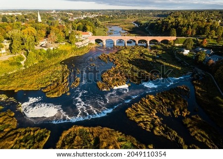 Venta Rapid waterfall, the widest waterfall in Europe and long red brick bridge in sunny autumn morning, Kuldiga, Latvia. Captured from above. Royalty-Free Stock Photo #2049110354