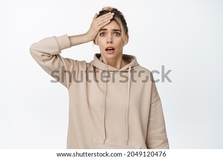 Worried young woman looking alarmed at camera, hold hand on head, forgot remember something, panicking, standing anxious against white background