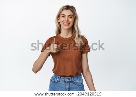 Positive feedback. Smiling blond girl shows thumbs up to approve or praise something. Young woman making compliment, recommending product, white background