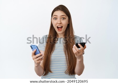 Excited and amazed young woman holding credit card and mobile phone, surprised reaction to special offer, discount at online shopping app, white background