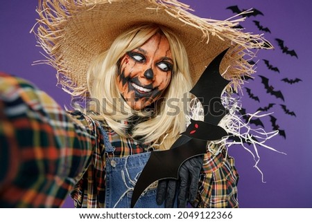 Close up fun young woman with Halloween makeup mask in straw hat scarecrow costume do selfie shot pov mobile phone hold bats isolated on plain dark purple background studio Celebration party concept