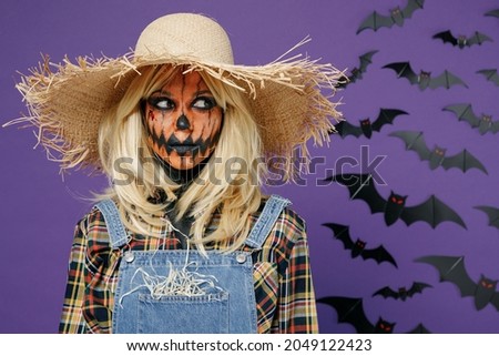 Young calm woman 20s with Halloween makeup mask wearing straw hat denim scarecrow costume look aside isolated on plain dark purple color background studio portrait Celebration holiday party concept