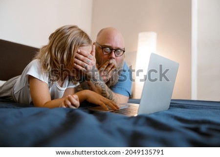Shocked father closes eyes of daughter to protect from dangerous content on laptop on bed