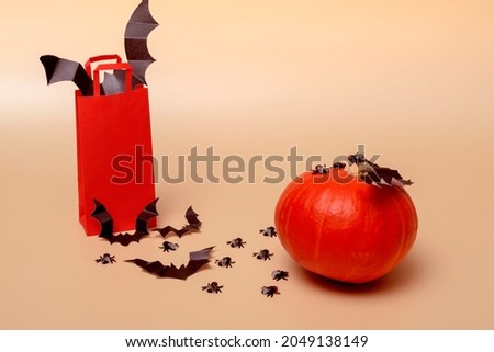Halloween party concept. On a beige background, a red package with bats, flies and pumpkin. With copy space close-up.