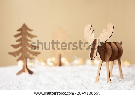 Christmas deer. Decorative wooden reindeer toy on pastel beige background. Happy new year 2022. Winter Greeting card with snow and light. Handmade figure deer and fir tree. Eco style diy. Copy space.