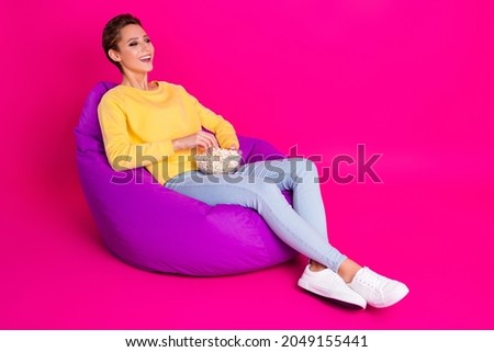 Photo of adorable shiny young woman dressed yellow pullover sitting bean eating pop corn smiling isolated pink color background
