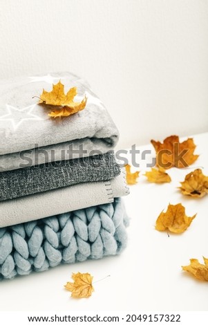 Stack of gray woolen knitted blankets on white table, warm plaids decorated maple leaves, autumn cozy concept