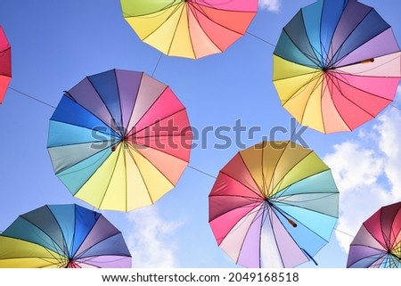 Colorful umbrellas in the colors of the rainbow hang in the air next to each other against a blue sky