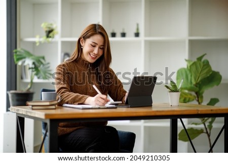 Portrait of Young Asian woman hand freelancer is working her job on computer tablet in modern office. Doing accounting analysis report real estate investment data, Financial and tax systems concept. Royalty-Free Stock Photo #2049210305